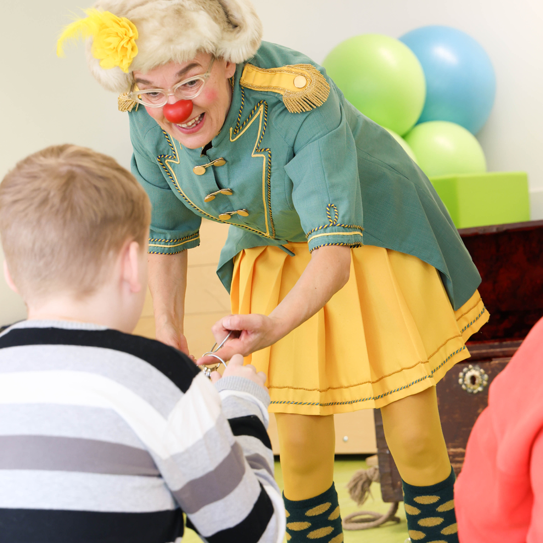 ROTE NASEN-Clownin Zitronella überreicht einem Kind einen Gegenstand.
